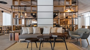 Un intérieur moderne avec un canapé, deux tables rondes et une chaise. On y trouve également des étagères et un luminaire suspendu.