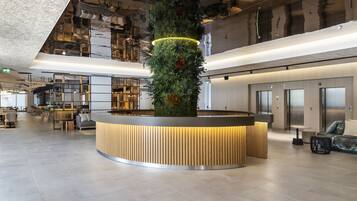 A modern lobby with a central reception desk, a vertical garden, and a mezzanine level with seating.