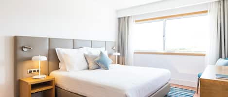 Een moderne hotelkamer met een groot bed, een nachtkastje met een lamp, een bureau en een raam met gordijnen.