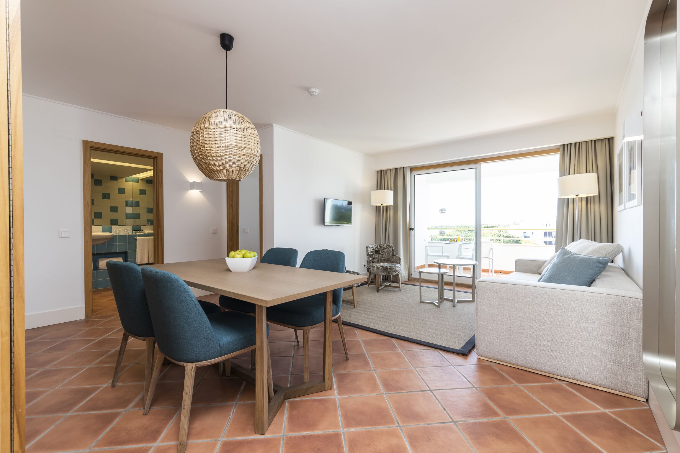 A modern hotel room with a dining area, a sofa, and a large window offering a view.