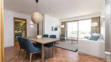 A modern hotel room with a dining area, a sofa, and a large window offering a view.