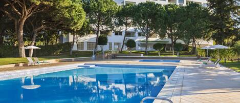 A swimming pool with a clear blue water, surrounded by trees and a building in the background.
