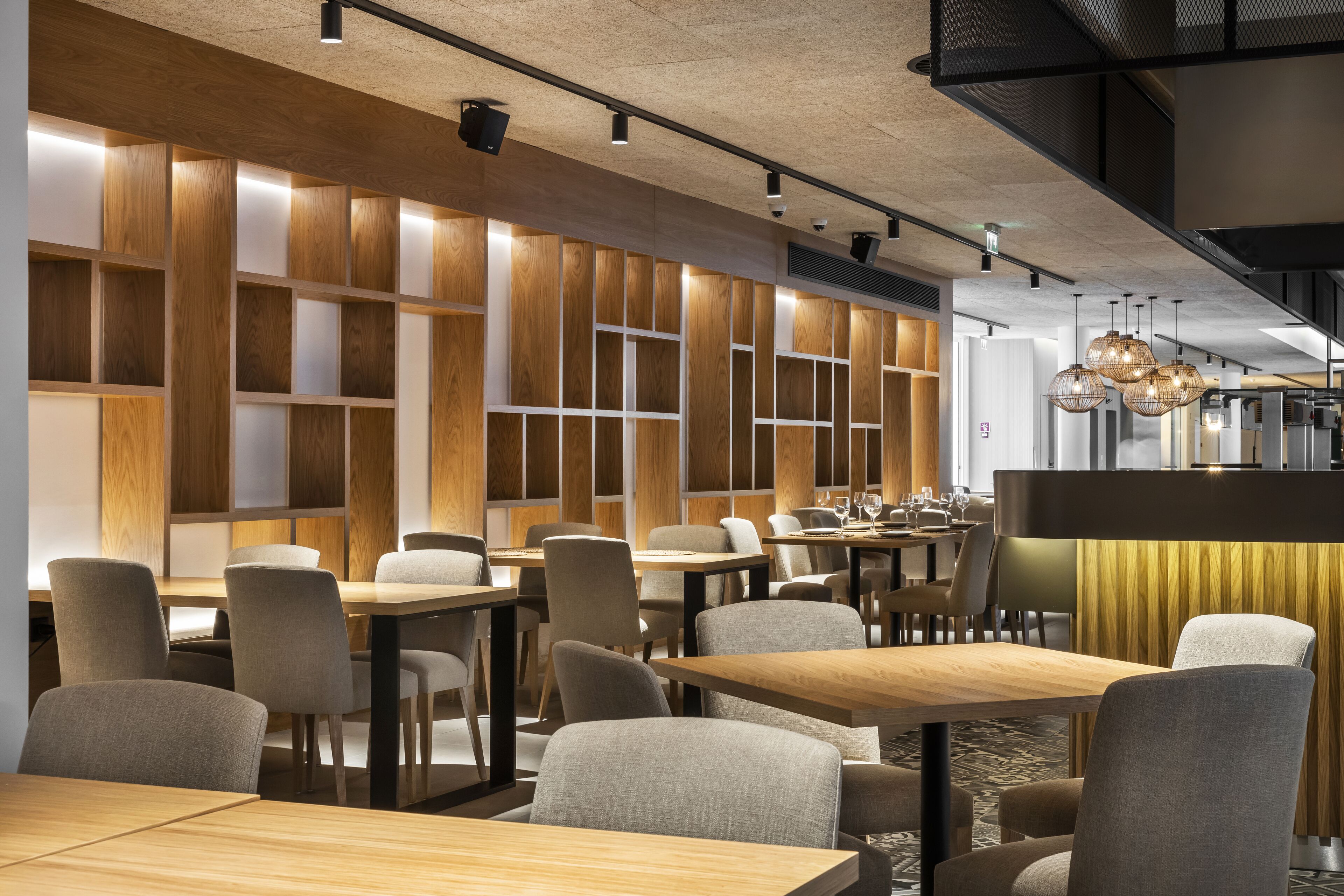 Interior de restaurant modern amb parets de panells de fusta, diverses taules i cadires, i lluminàries penjants.