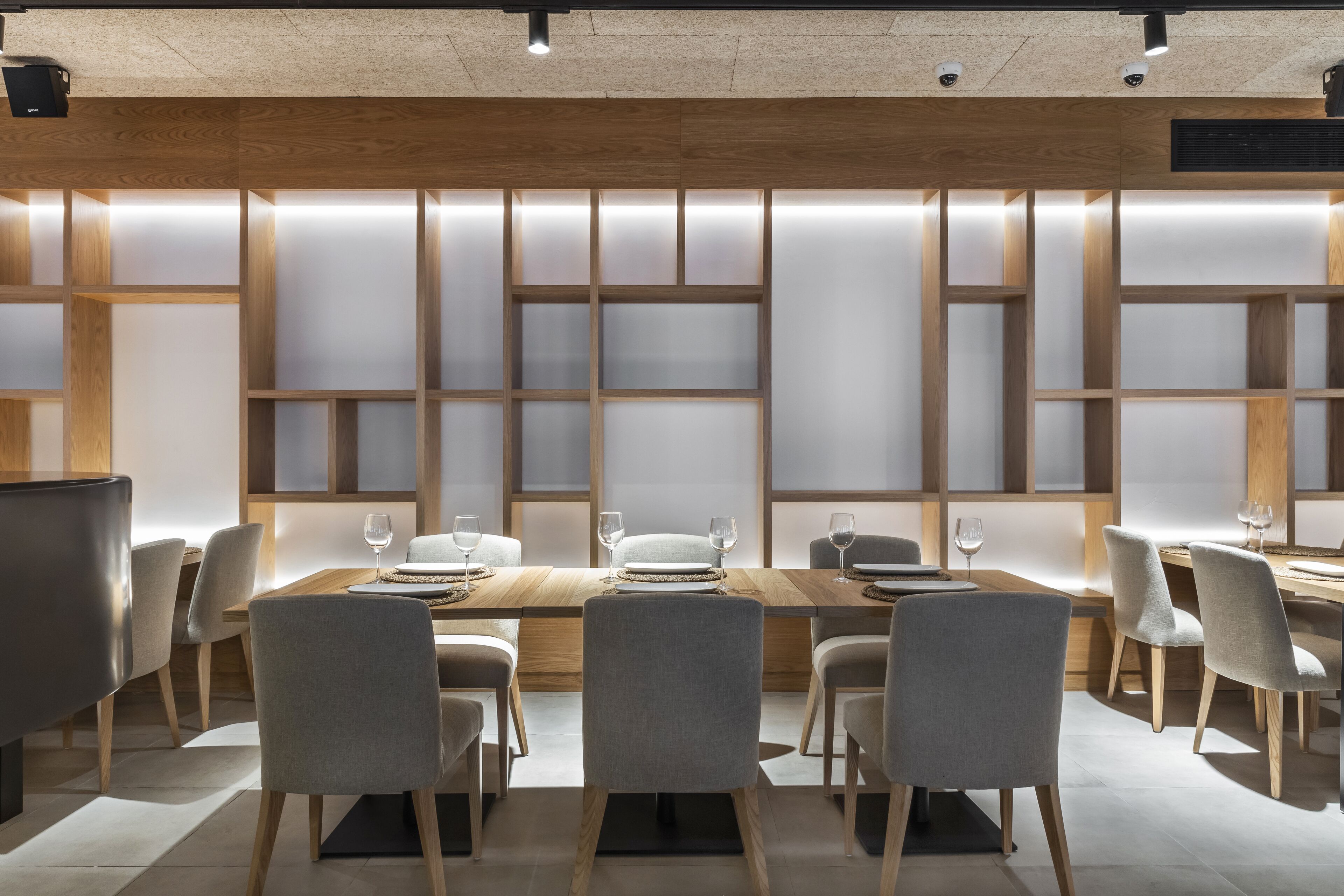 Un comedor moderno con una mesa y sillas de madera, iluminación empotrada y vistas de la ciudad a través de amplios ventanales.