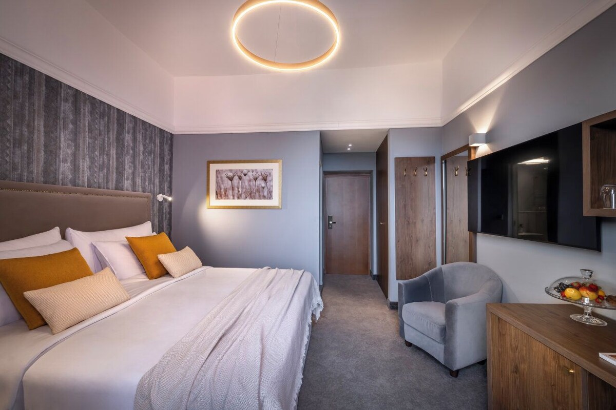 Una habitación de hotel con cama, una silla, escritorio y televisor montado en la pared.