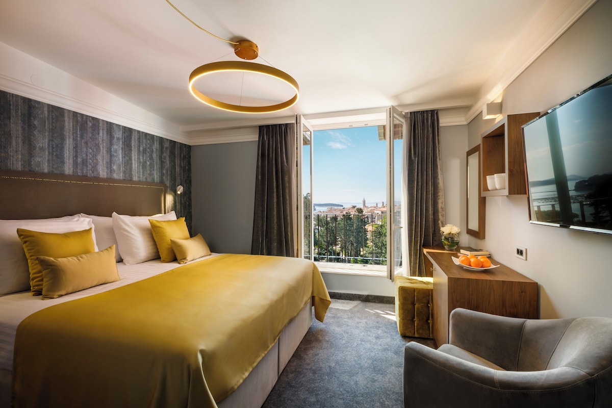 Habitación de hotel con una cama grande, un escritorio con televisor y vistas a la ciudad.
