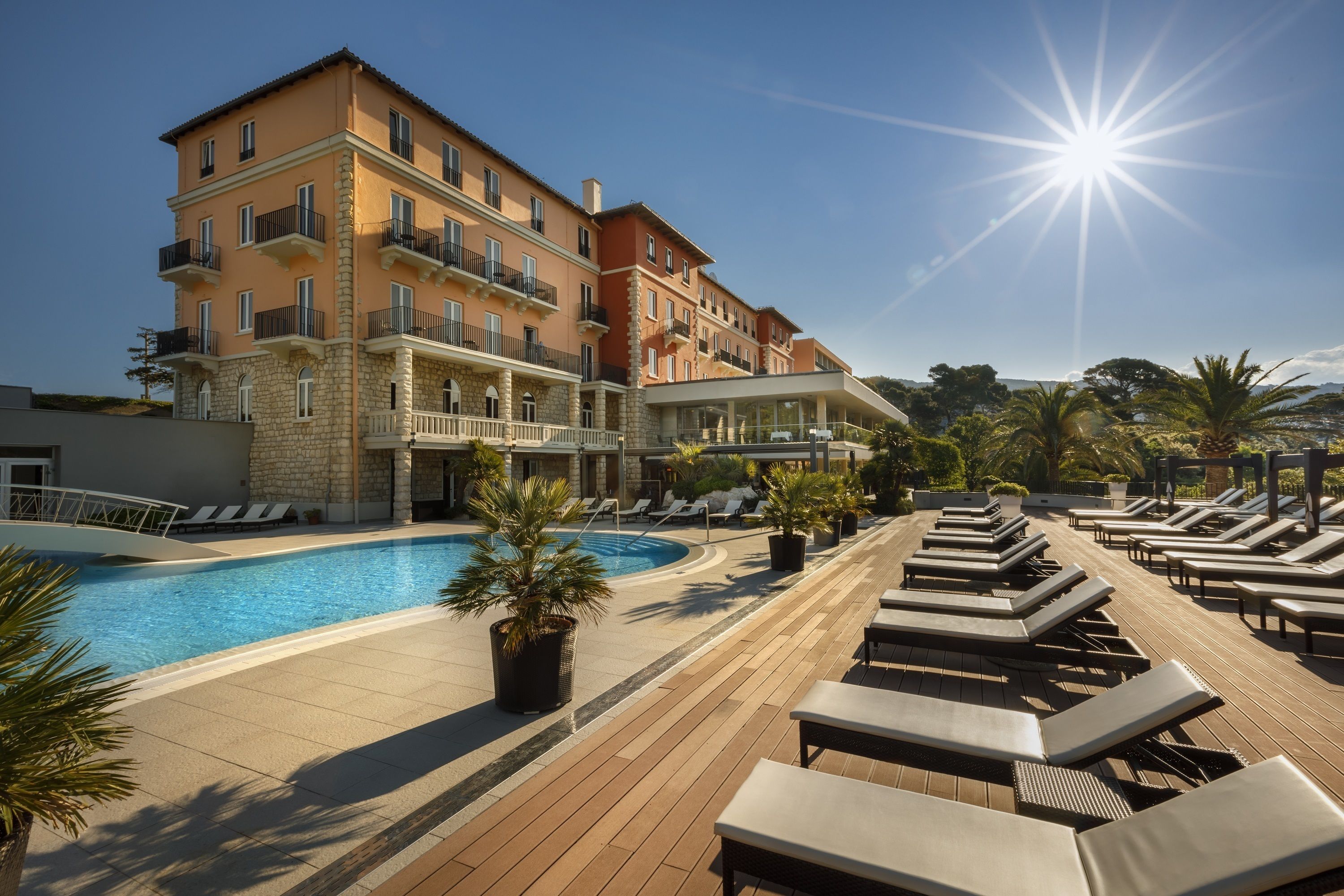 A hotel with a pool, sun loungers, and a clear sky.
