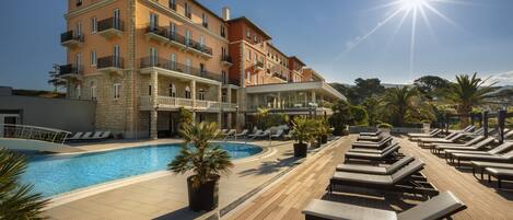 A hotel with a pool, sun loungers, and a clear sky.