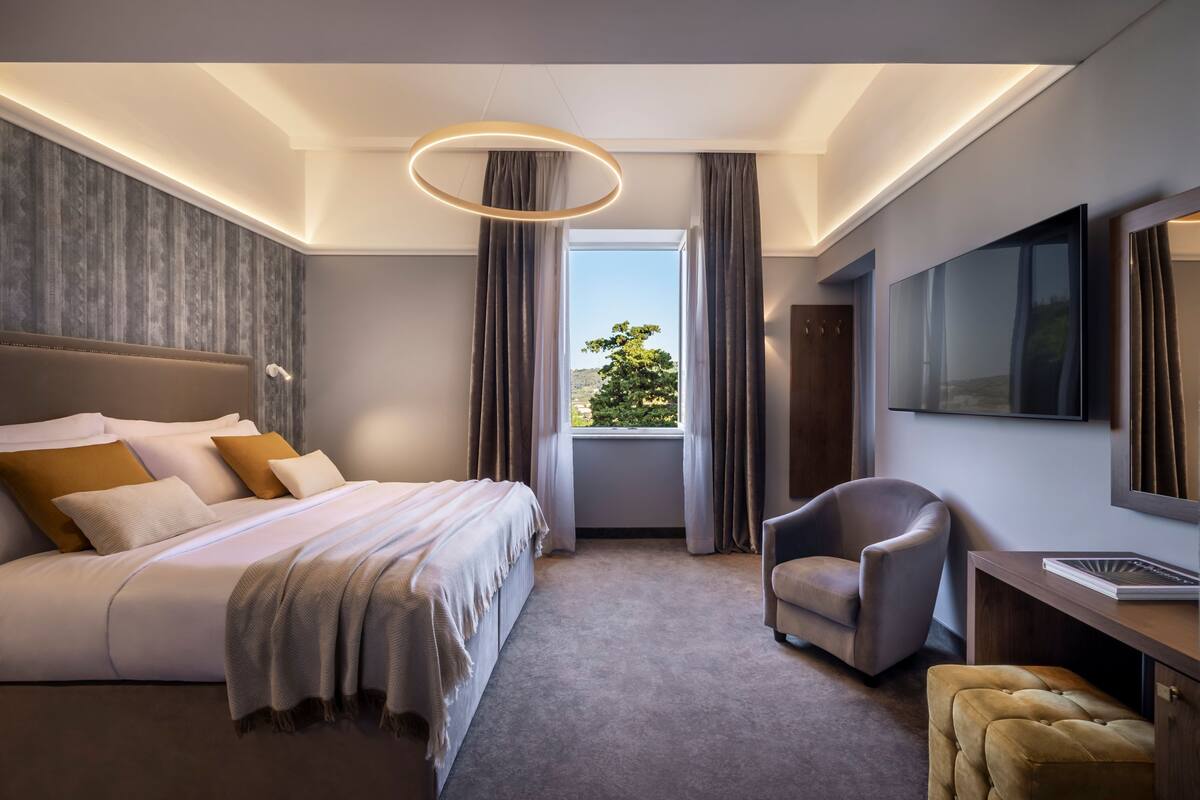 A modern hotel room with a large bed, a seating area, and a TV.