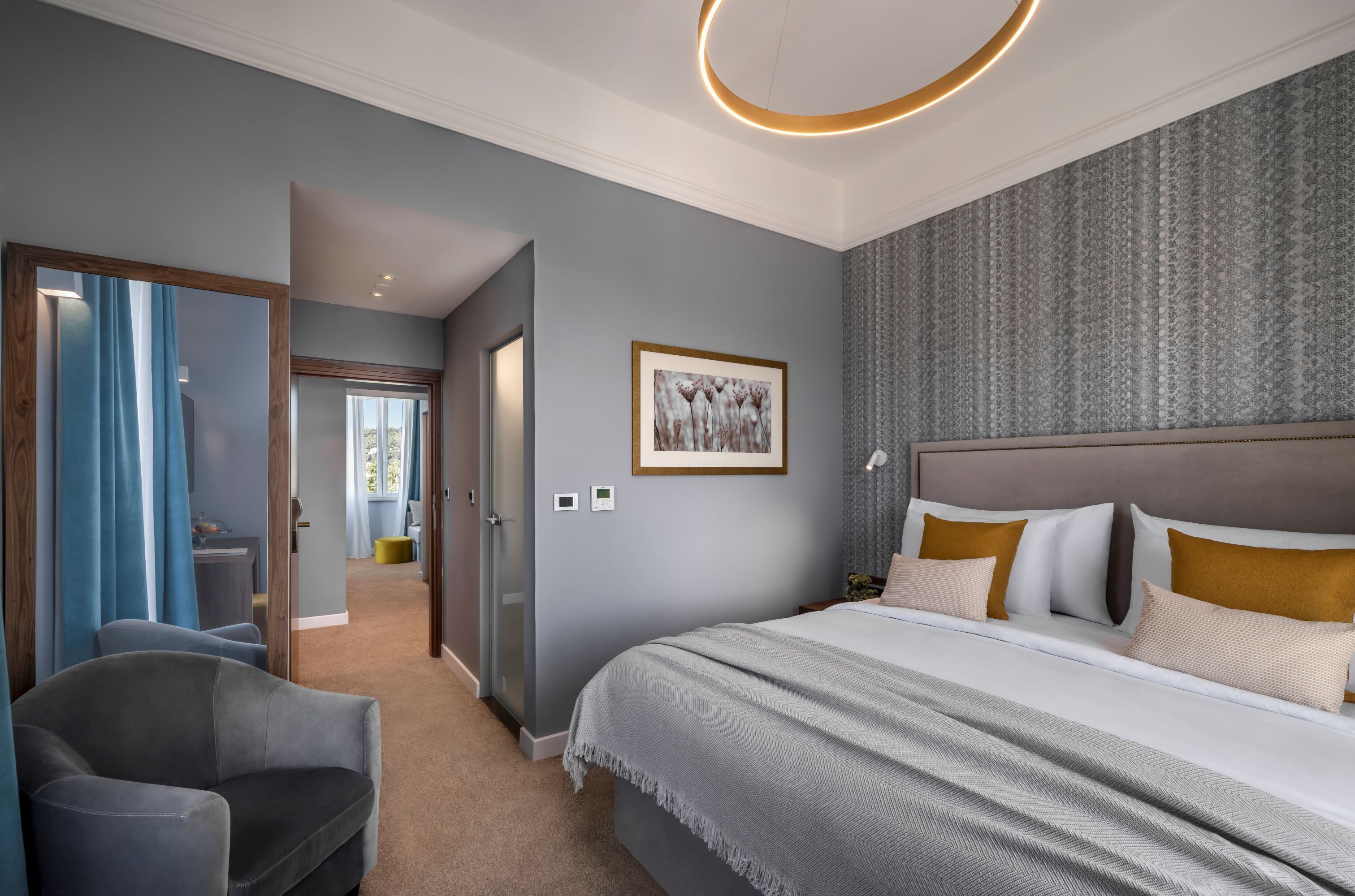 Ein modernes Hotelzimmer mit einem großen Bett, einer Sitzecke und Blick auf den Flur.