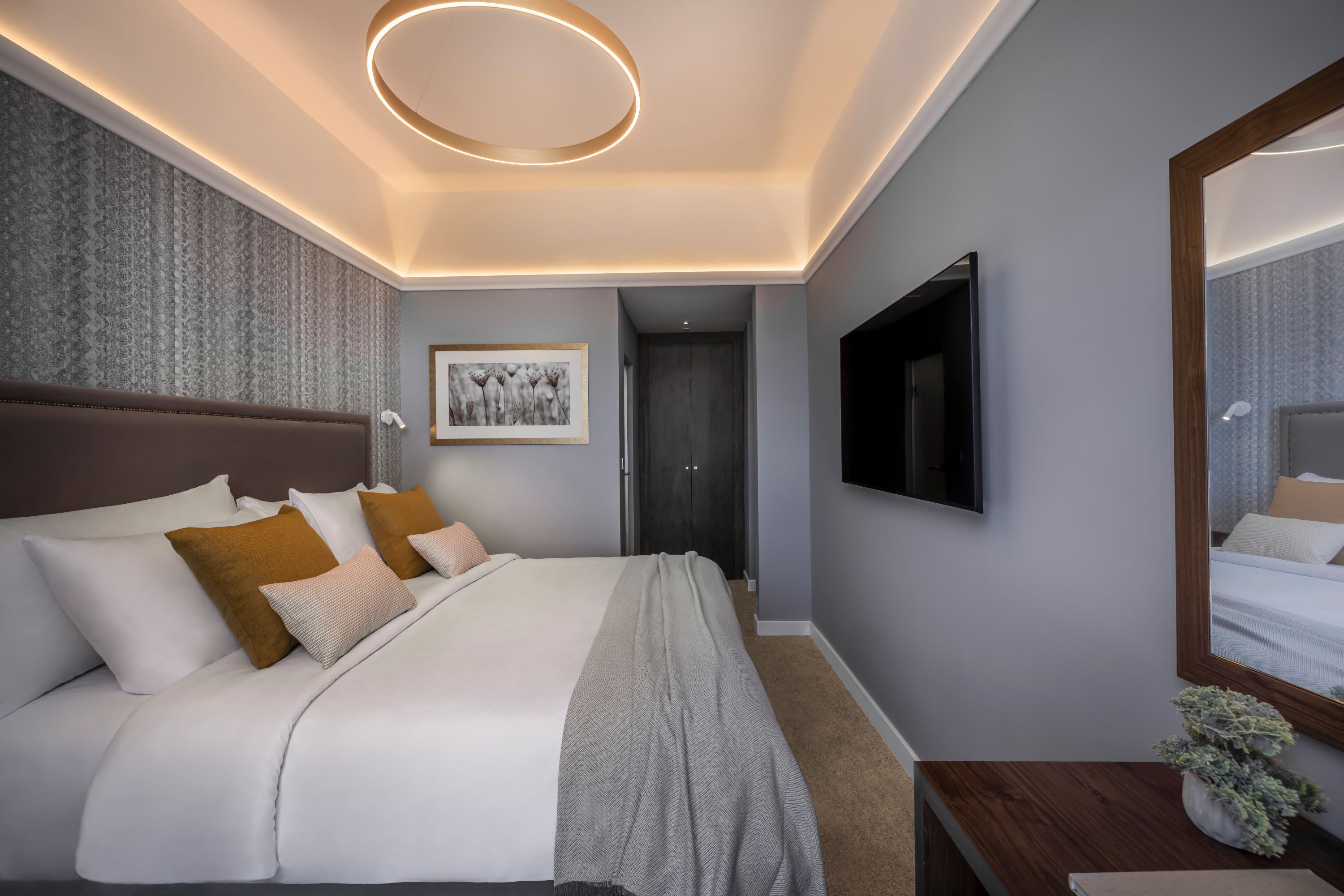 A modern bedroom with a large bed, a flat-screen TV, a mirror, and a framed artwork on the wall.