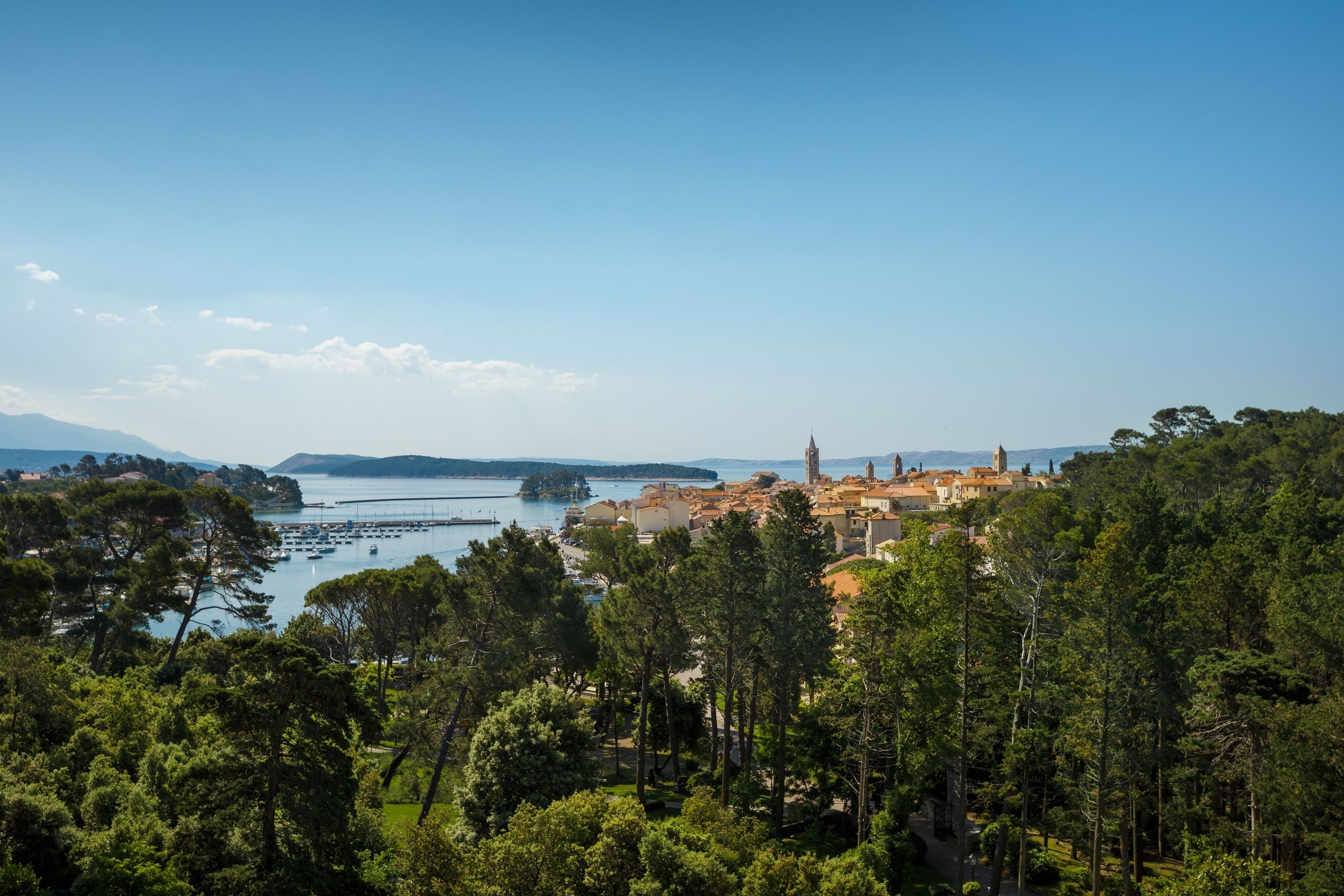 A coastal town with a prominent church, surrounded by dense greenery and a clear blue sky.