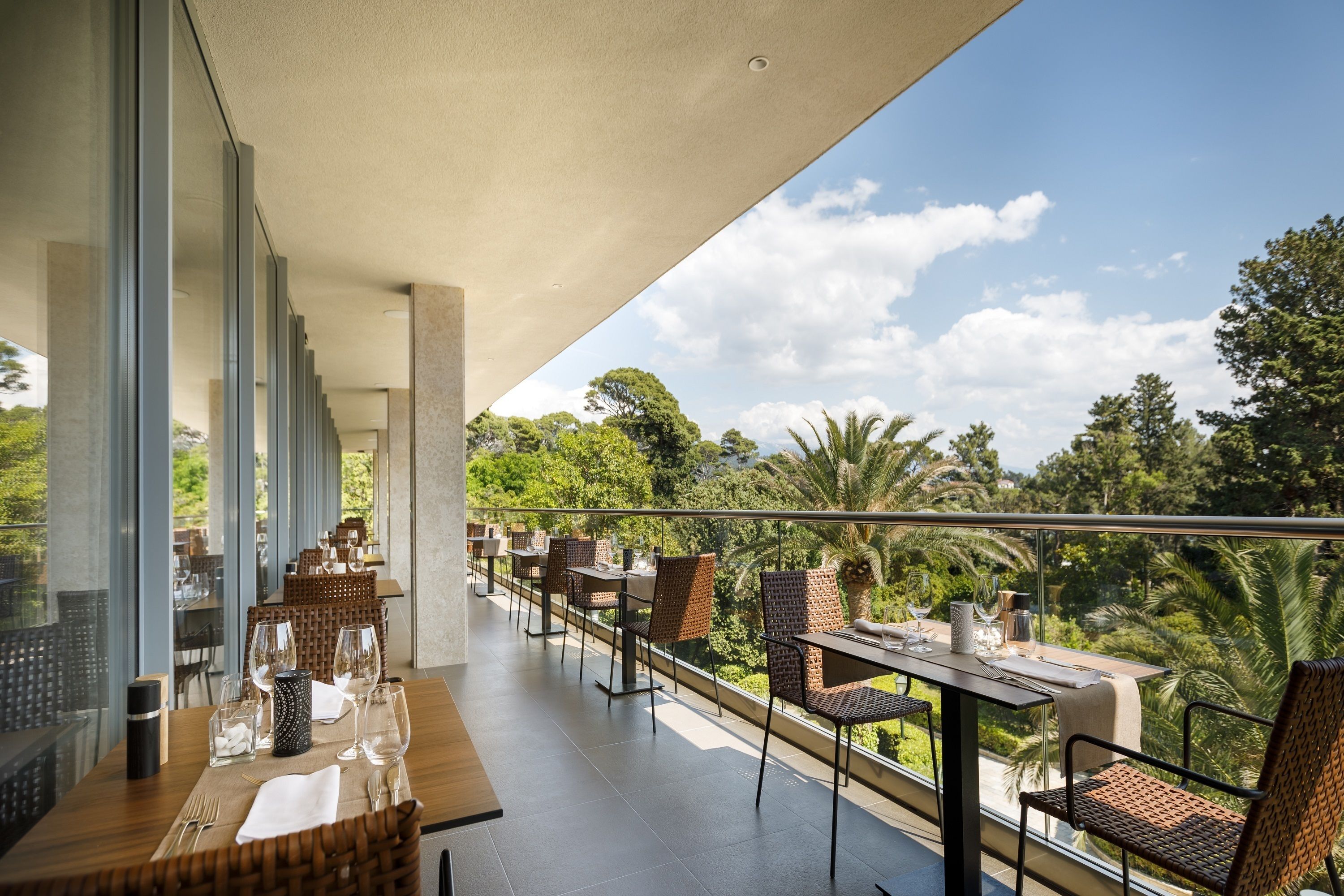 A dining area with tables and chairs, large windows, and a view of greenery.