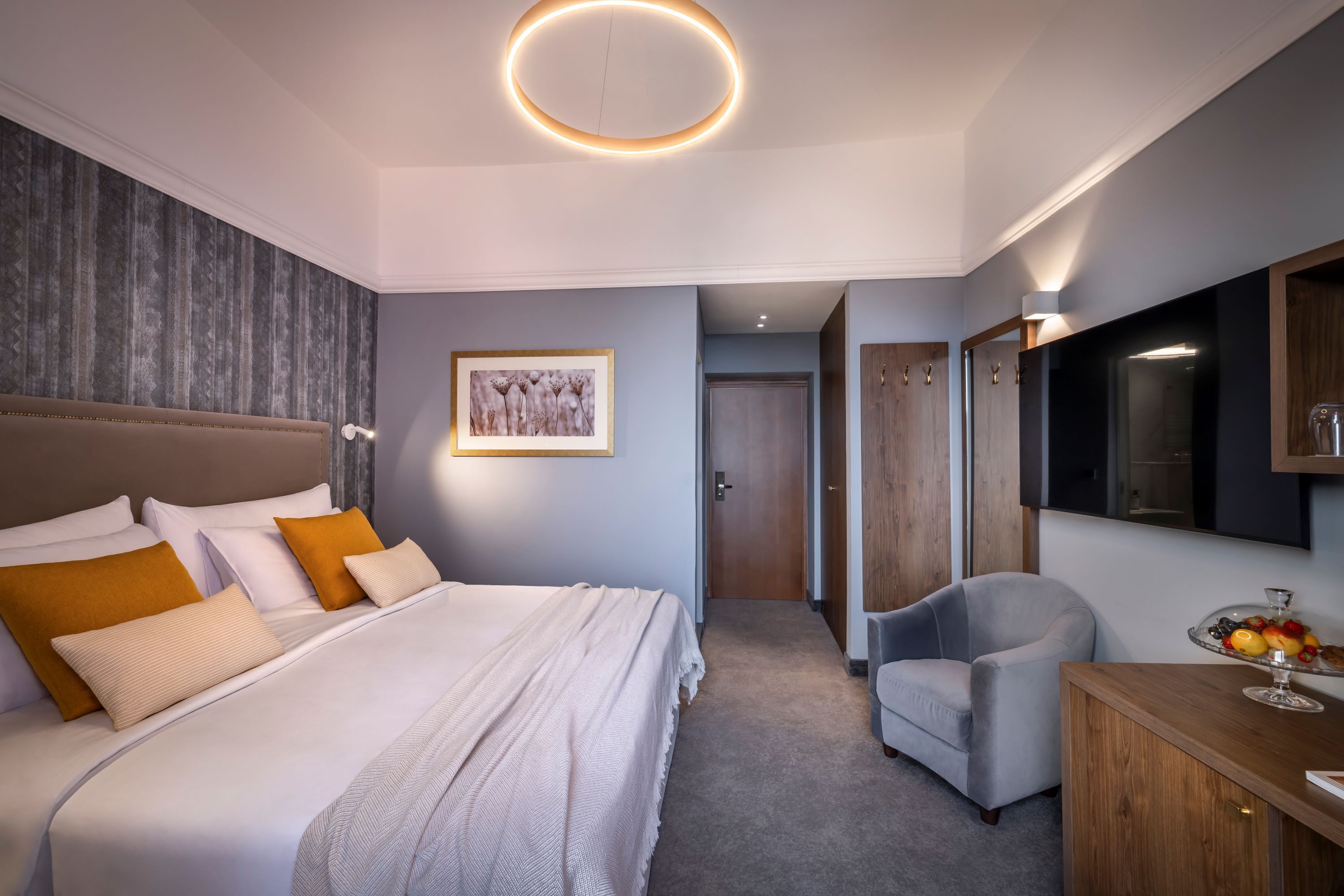 Una camera da letto moderna con un letto grande, una poltrona grigia, una cassettiera in legno e un quadro appeso al muro.