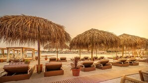 Een strandlounge met rieten parasols, houten ligbedden en potplanten.