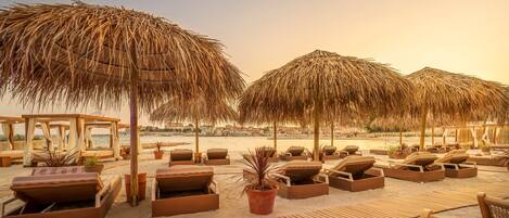 Een strandlounge met rieten parasols, houten ligbedden en potplanten.