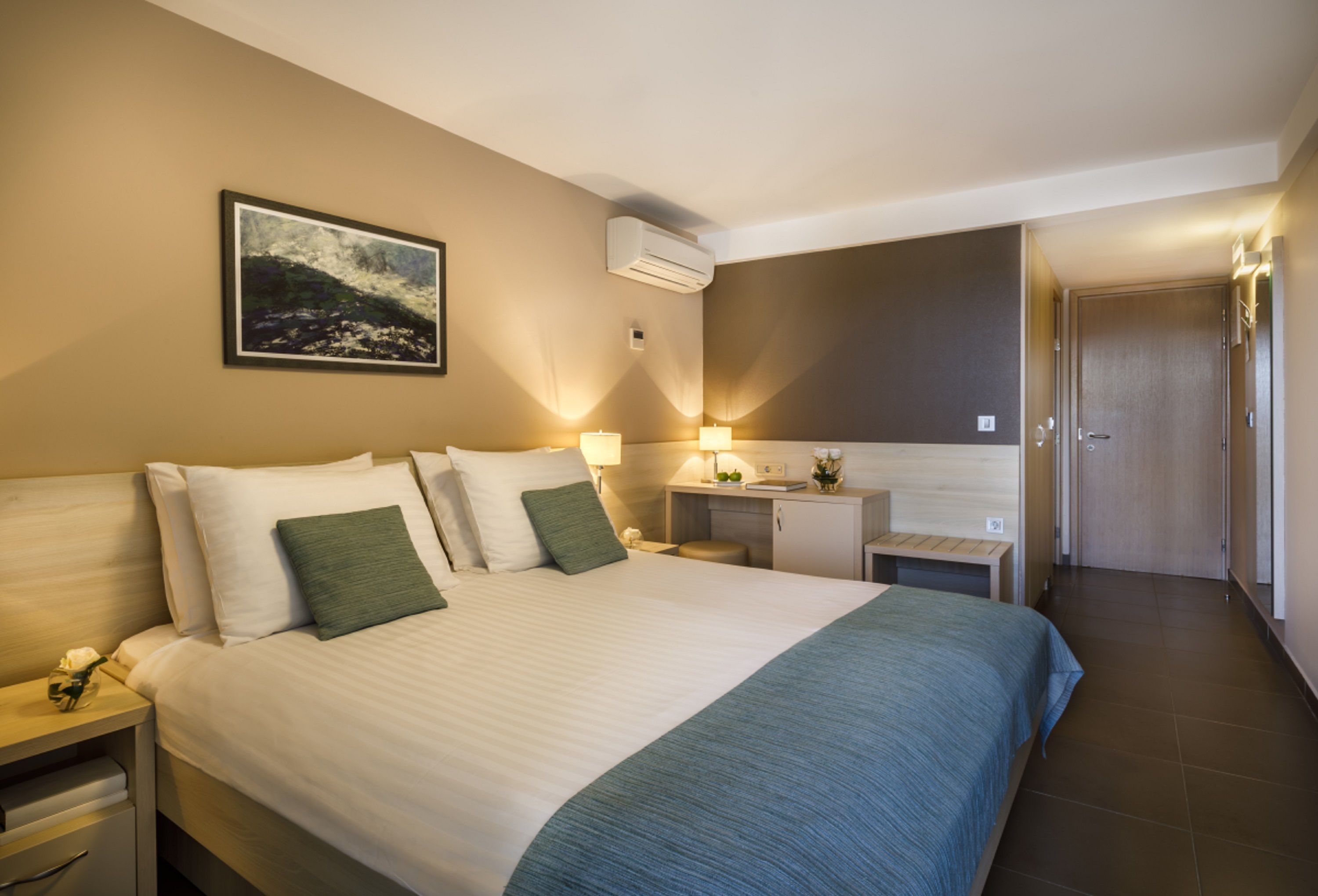 A hotel room with a large bed, bedside tables, a desk, and a door.