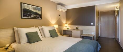 A hotel room with a large bed, bedside tables, a desk, and a door.