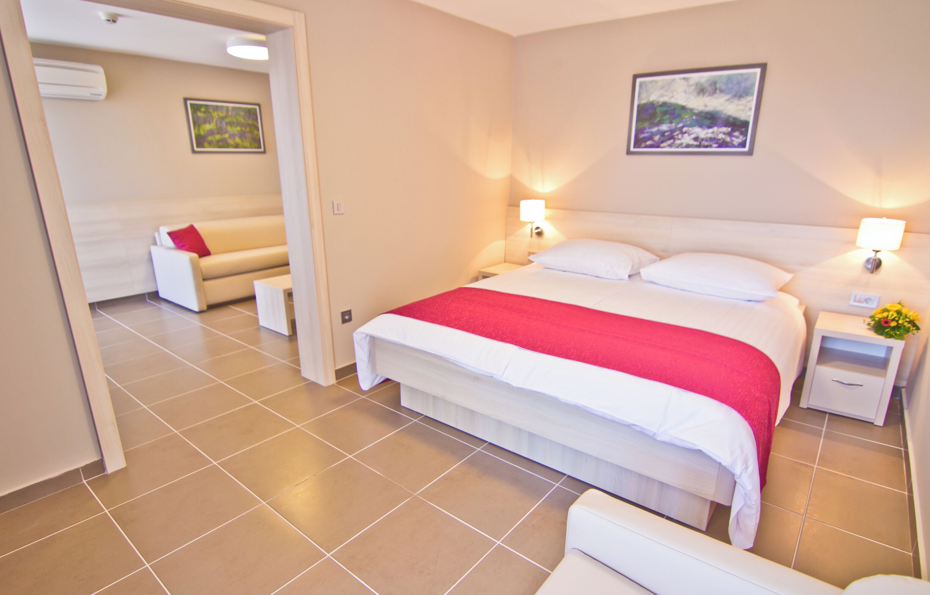 Een hotelkamer met een bed, nachtkastjes, een slaapbank en een schilderij aan de muur.