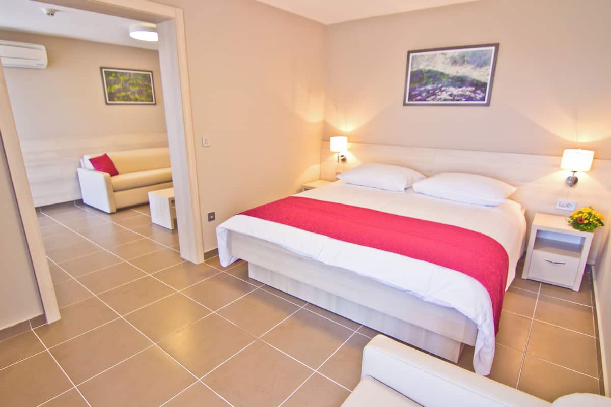 Ein Hotelzimmer mit Bett, Nachttischen, einer Schlafcouch und einem Gemälde an der Wand.