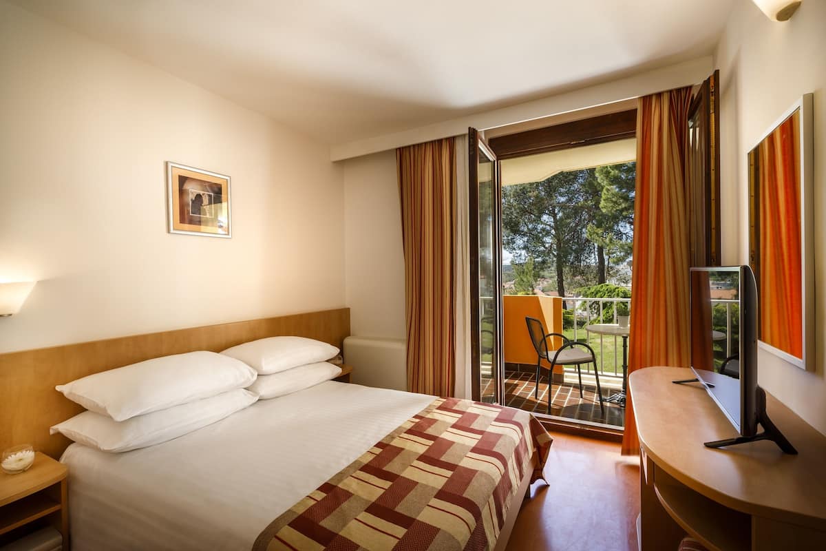 Une chambre d’hôtel avec un lit, un bureau, une chaise et un balcon avec des rideaux.