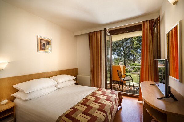 A hotel room with a bed, a desk, a chair, and a balcony with curtains.