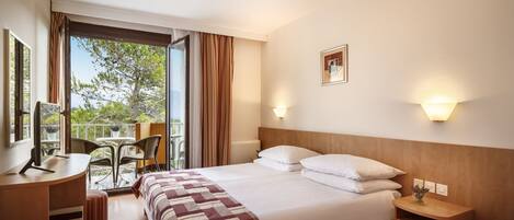 A hotel room with a bed, bedside table, lamp, and a view of the outdoors.