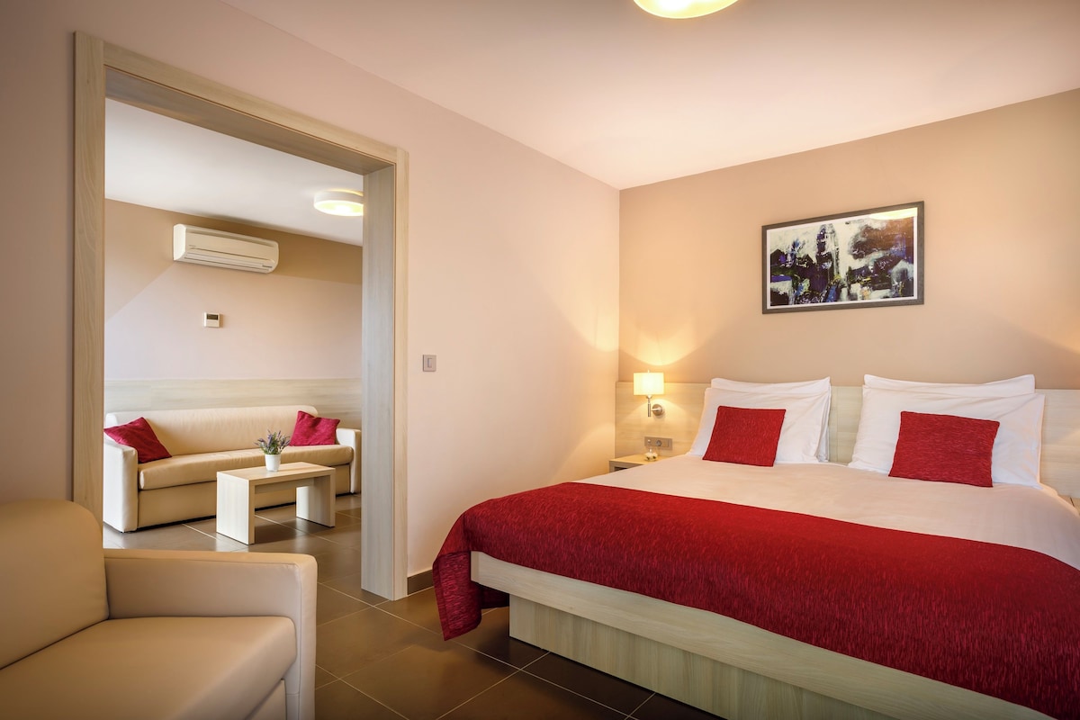 Une chambre d’hôtel avec un lit, un canapé, une table basse, une lampe et un tableau au mur.