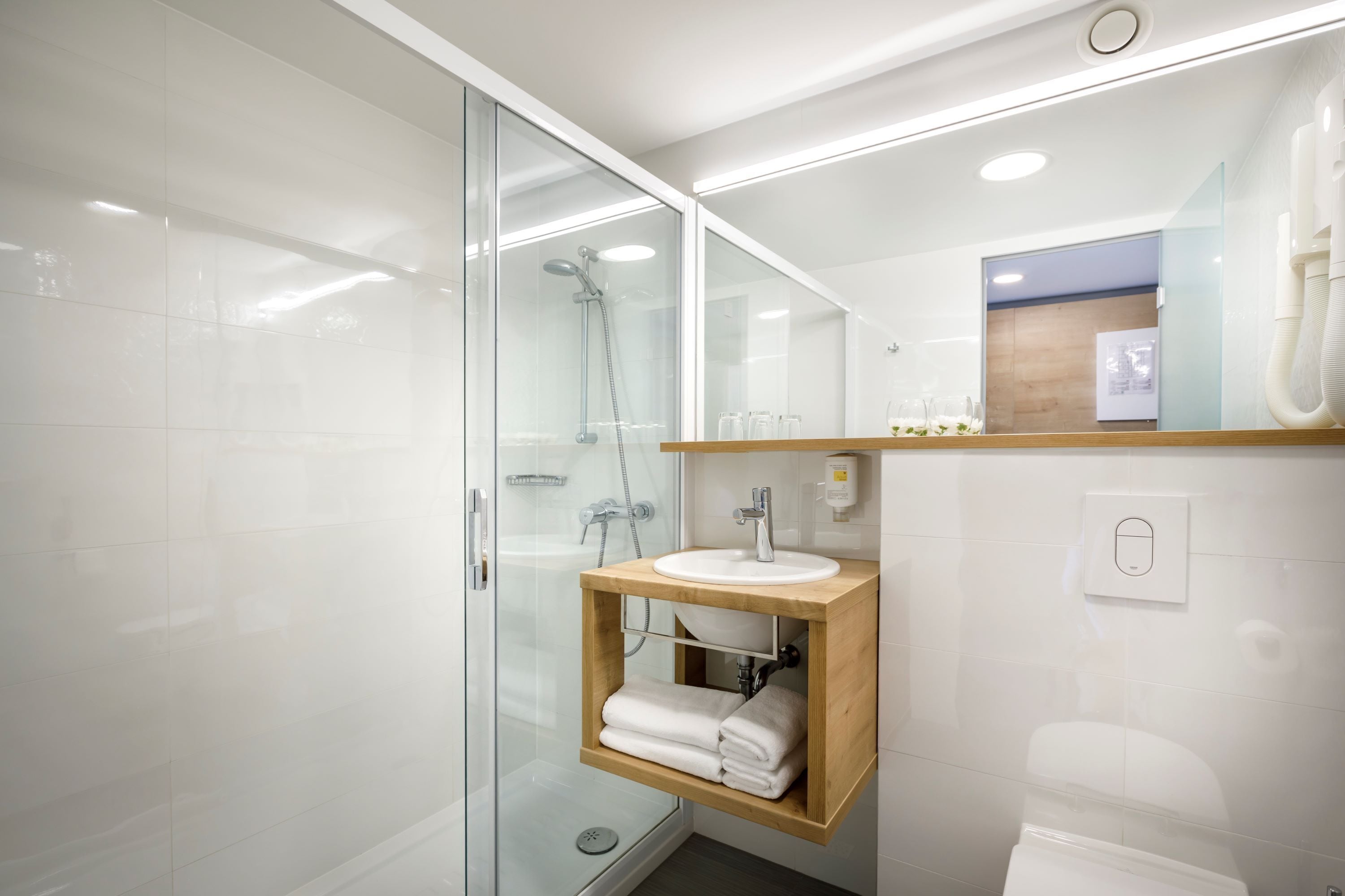 Une salle de bain moderne dotée d’une douche à parois de verre, d’un meuble-lavabo en bois et d’un miroir placé au-dessus du meuble-lavabo.