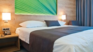 Hotelkamer met een bed, bedlampjes, een telefoon en een groot kunstwerk van een groen blad aan de muur.