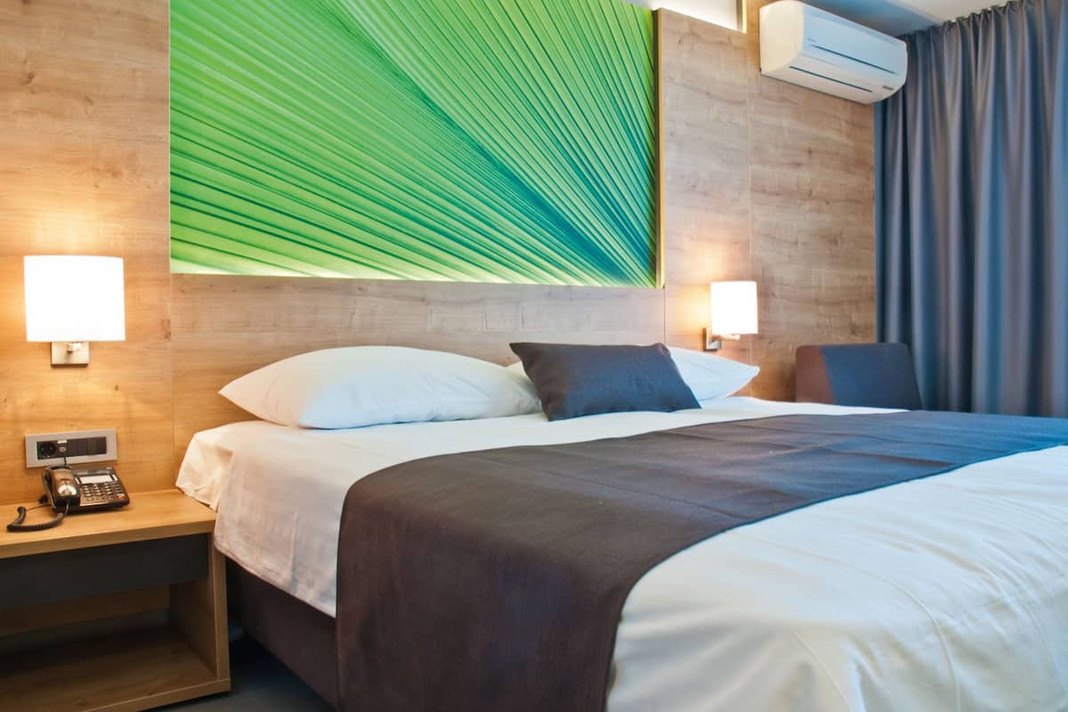 Une chambre d’hôtel avec un lit, des lampes de chevet, un téléphone et une grande œuvre d’art représentant une feuille verte au mur.