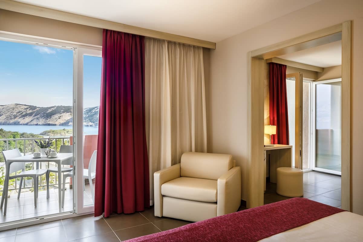 Une chambre d’hôtel avec un balcon, une chaise, un lit et un bureau avec une lampe.