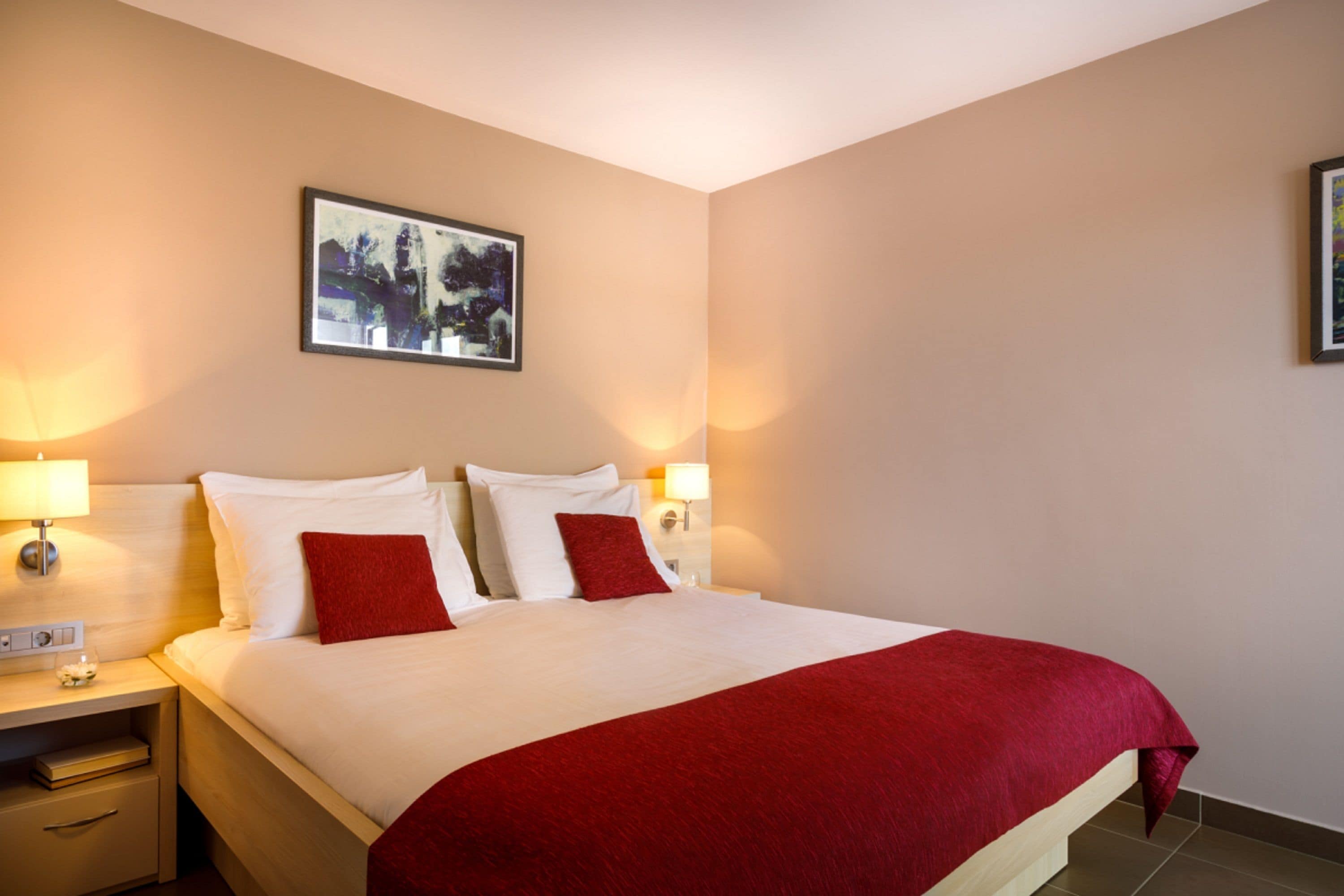 A hotel room with a large bed, two bedside lamps, a nightstand, and a framed picture on the wall.