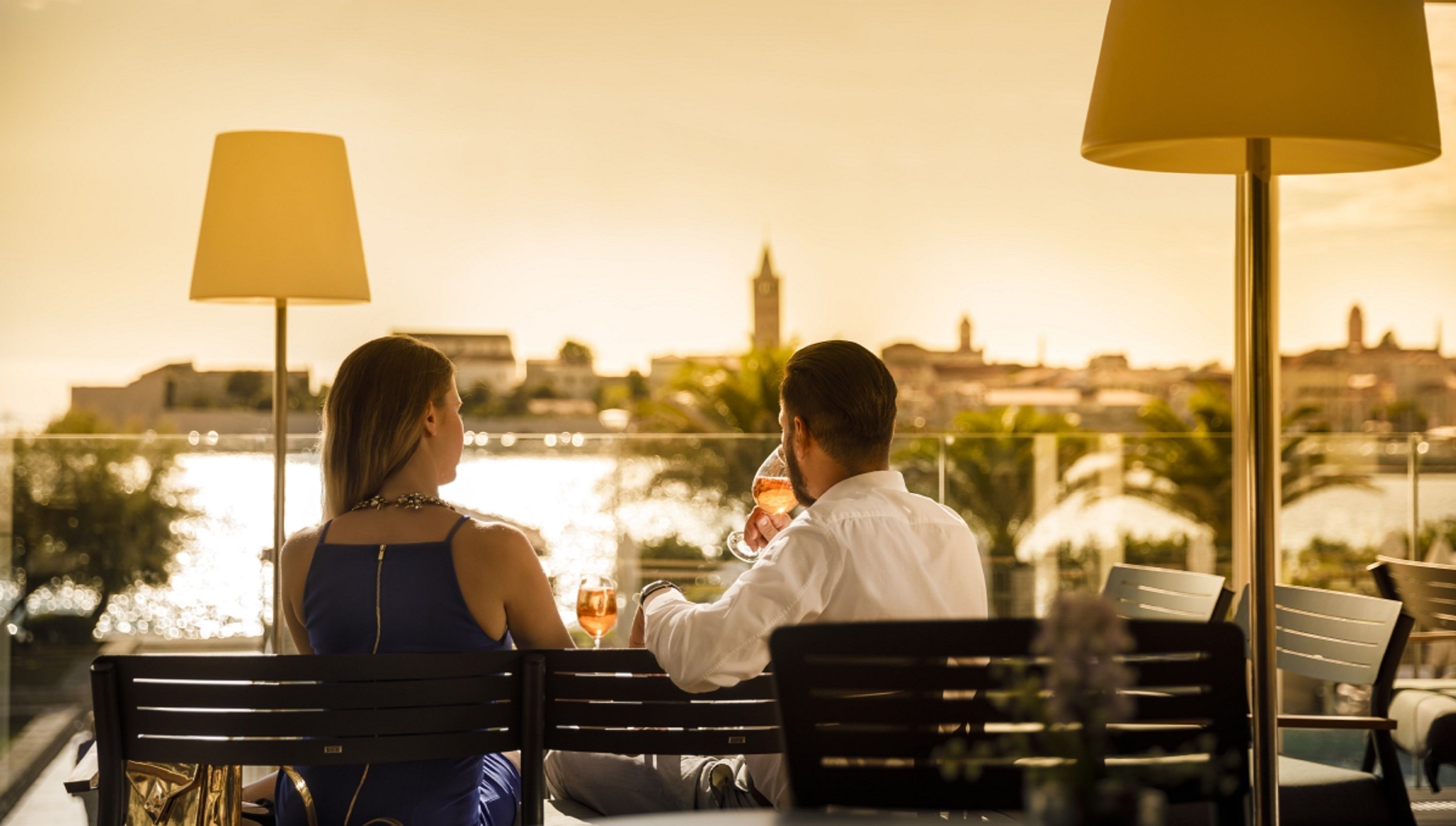 Two people sitting at a table with a view of a body of water and buildings in the background.