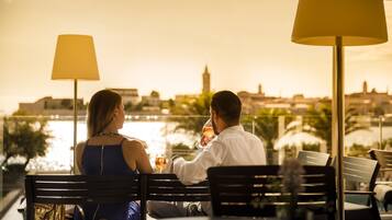 Two people sitting at a table with a view of a body of water and buildings in the background.
