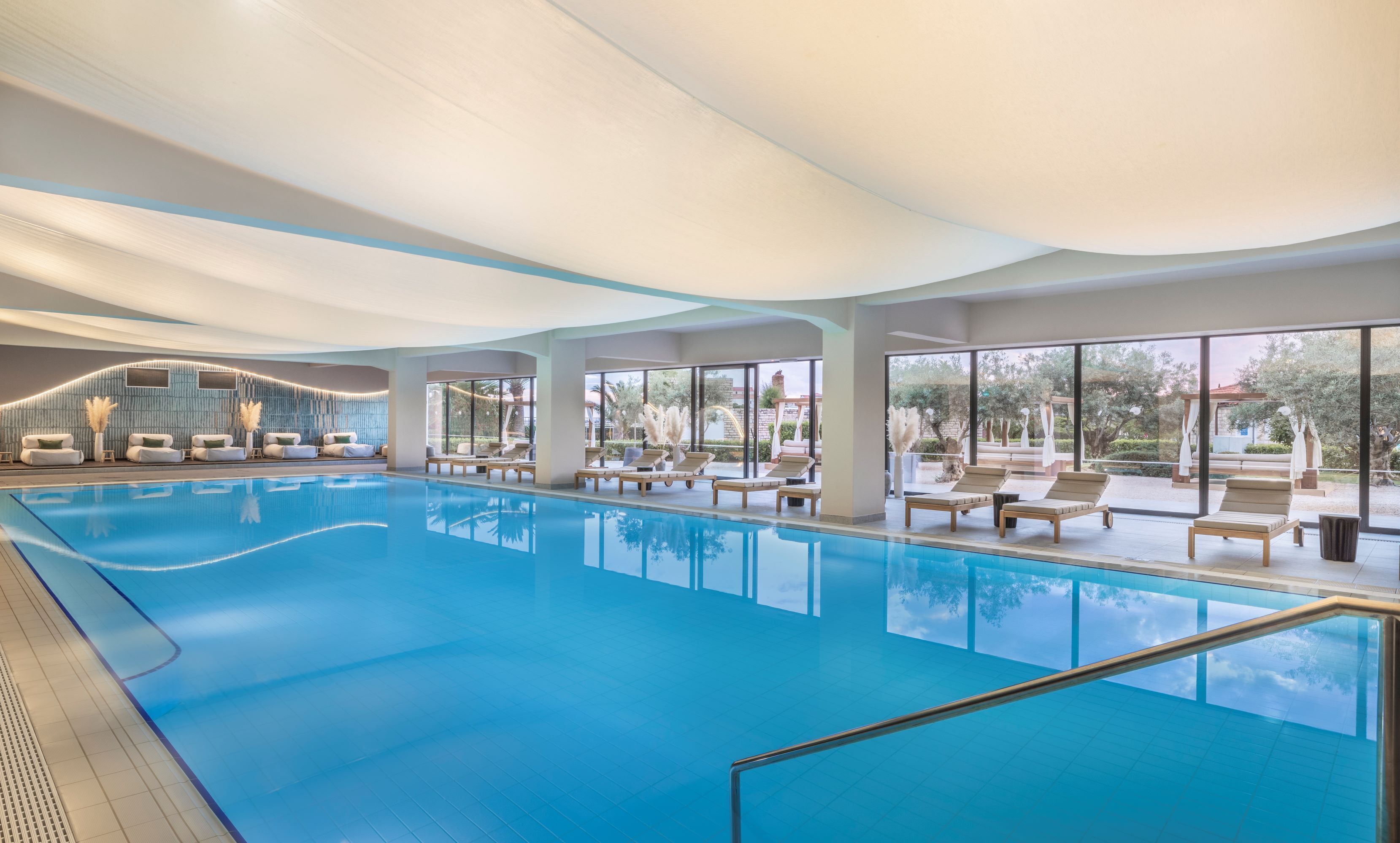 A large indoor swimming pool with lounge chairs and a view of the outdoors.