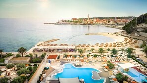 Un complejo turístico frente al mar con piscina, sombrillas de playa y vistas al océano y a la ciudad.