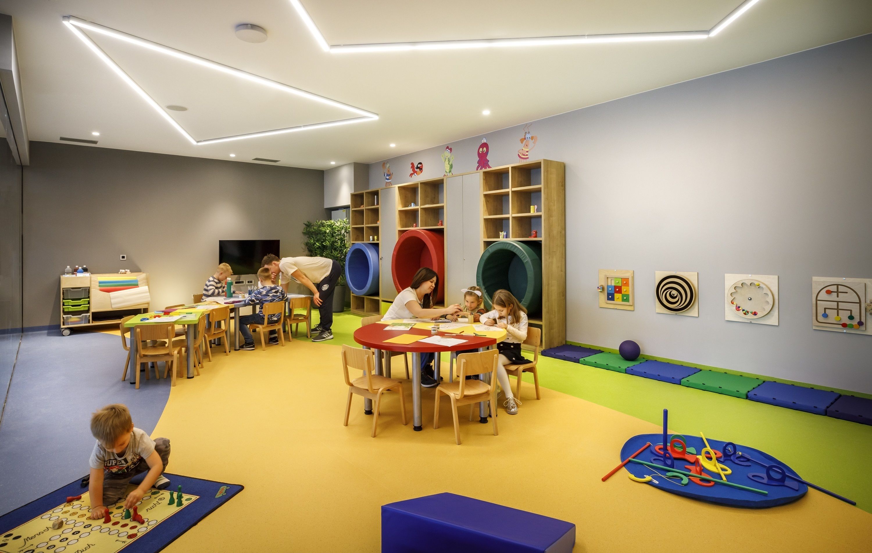 Zona infantil con mesas, sillas y alfombras de juego coloridas.