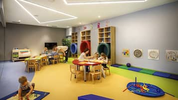 Zona infantil con mesas, sillas y alfombras de juego coloridas.