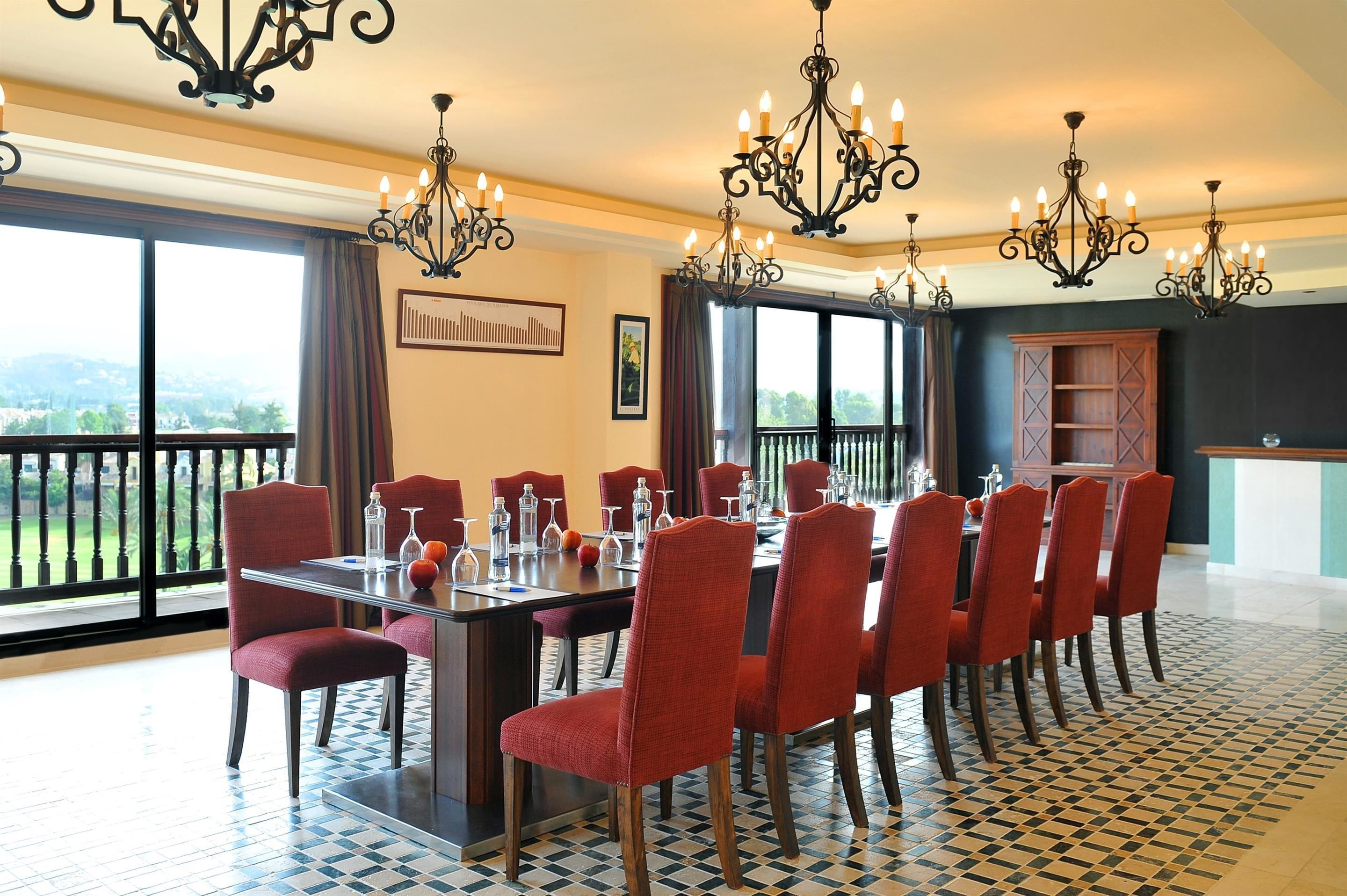 Een eetgedeelte met een grote tafel, rode stoelen en meerdere kroonluchters.