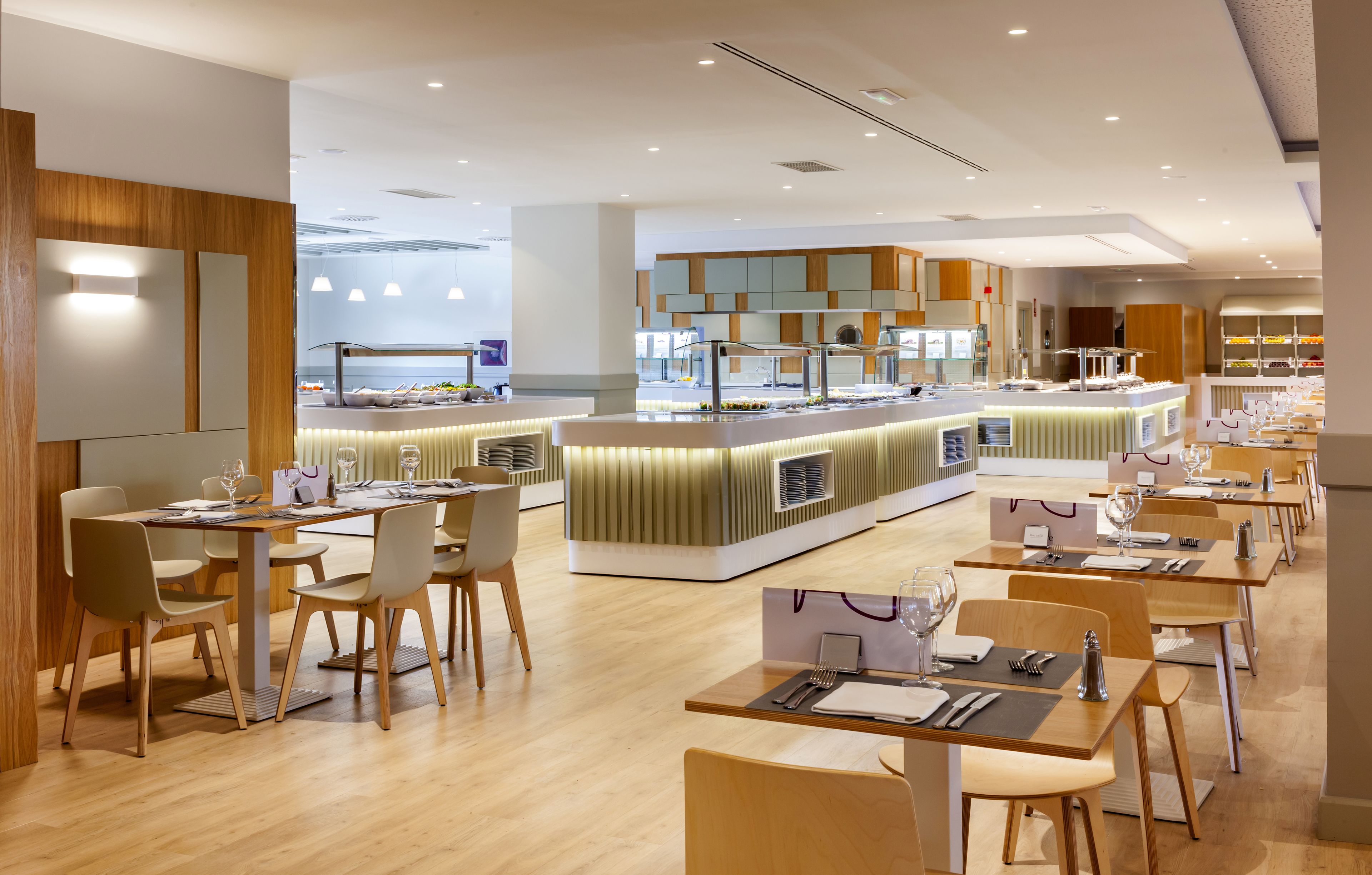 Ein modernes Restaurant mit Holzboden, mehreren Tischen und einer zentralen Theke mit verschiedenen Speisen.