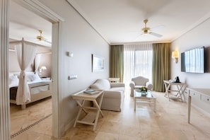 A hotel room with a bed, a sitting area with a sofa and armchairs, a coffee table, a TV, and a ceiling fan.