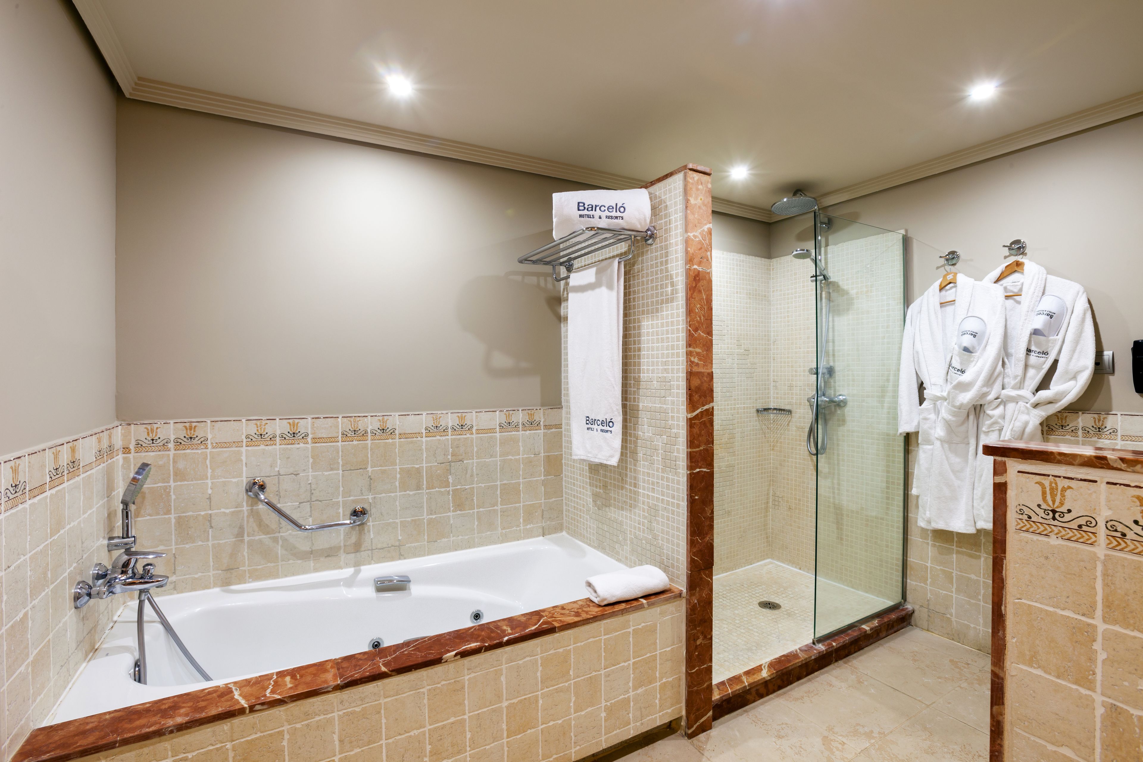 Un baño moderno con una bañera grande, una ducha con cerramiento de vidrio y dos albornoces blancos colgados en ganchos.