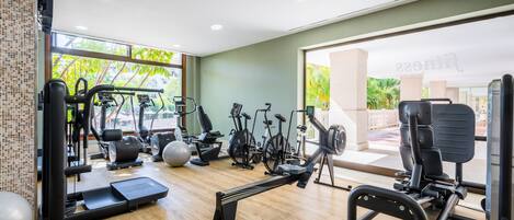 A gym with various exercise equipment, a large window, and a view of greenery outside.