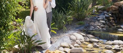 A couple standing by a small waterfall in a garden with rocks and greenery.