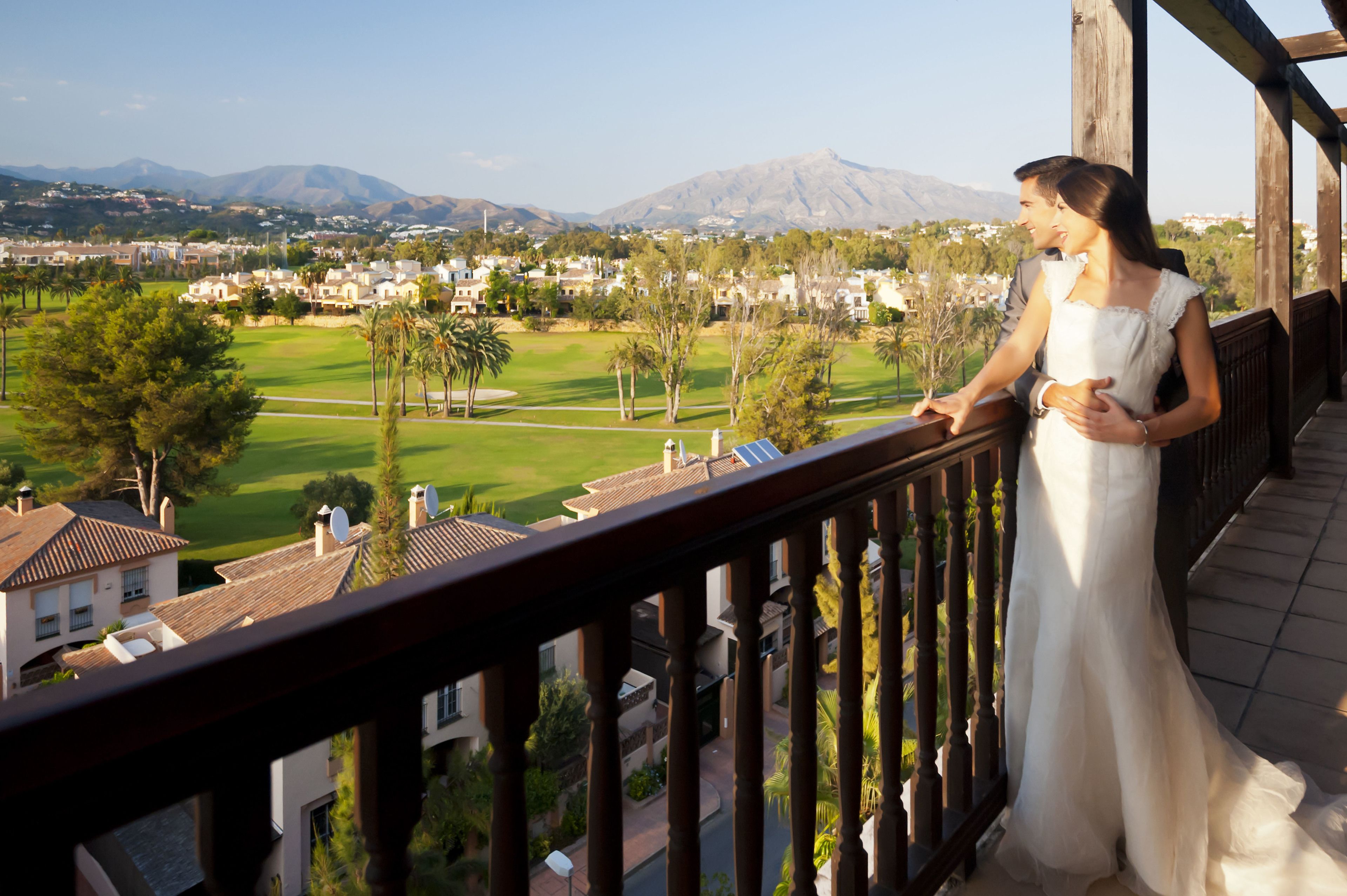 A balcony with a view of a golf course, houses, and mountains.