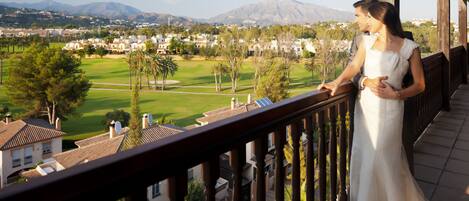 A balcony with a view of a golf course, houses, and mountains.