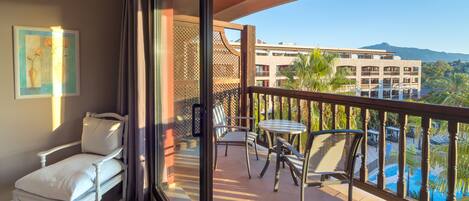 A balcony with a white chair, a small table, and a view of a building and mountains.