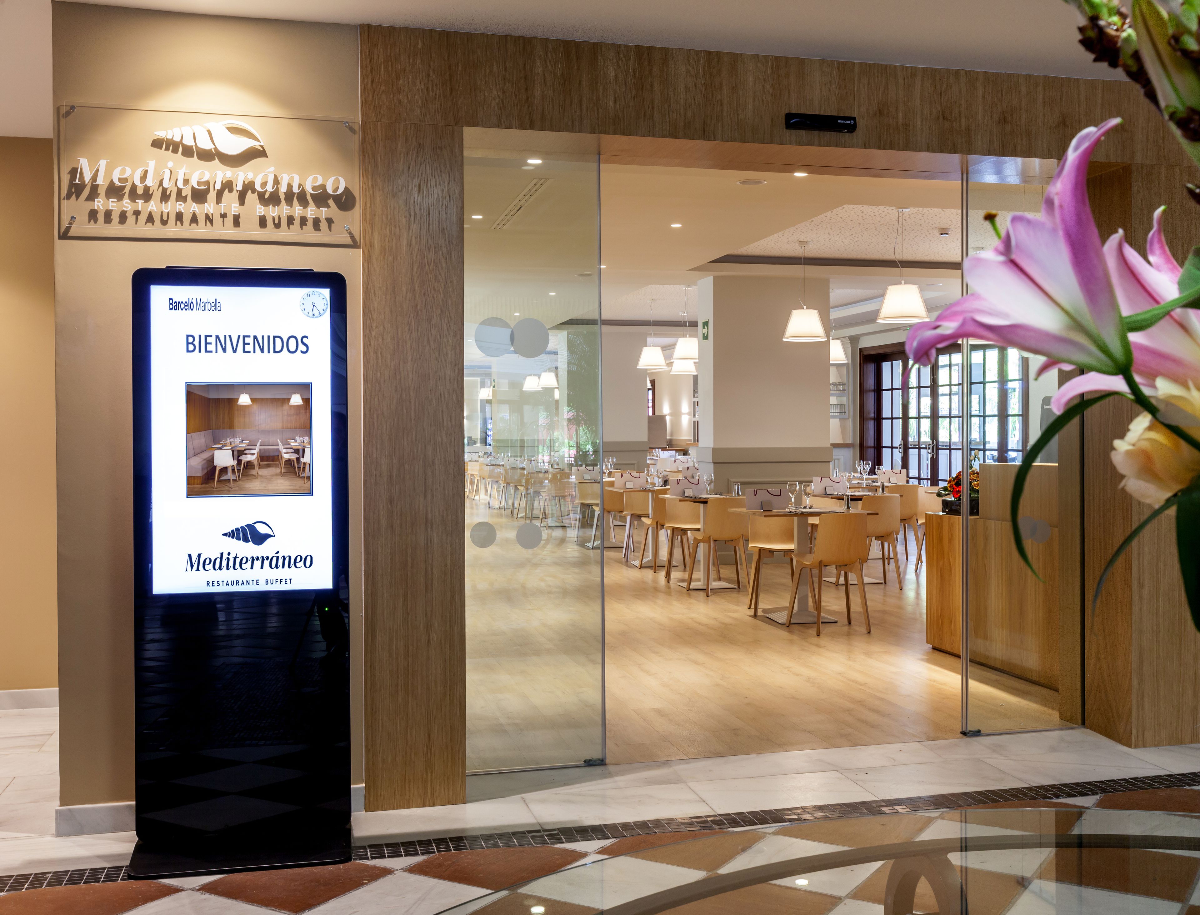 Un restaurante con un letrero digital de bienvenida, interiores de madera y vistas al salón.