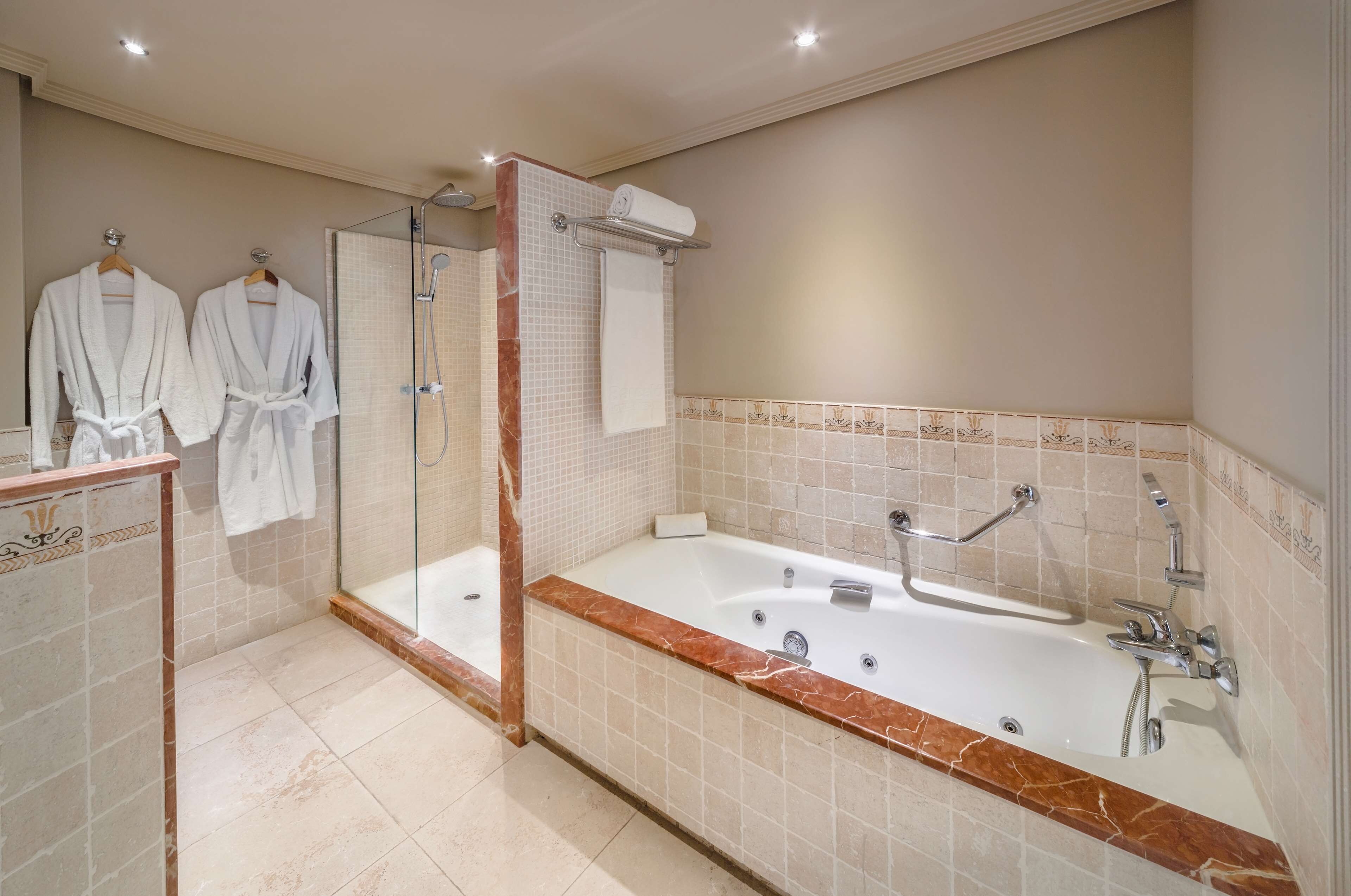 Une salle de bain moderne avec une grande baignoire, une douche à parois de verre et deux peignoirs blancs suspendus à un porte-serviettes.